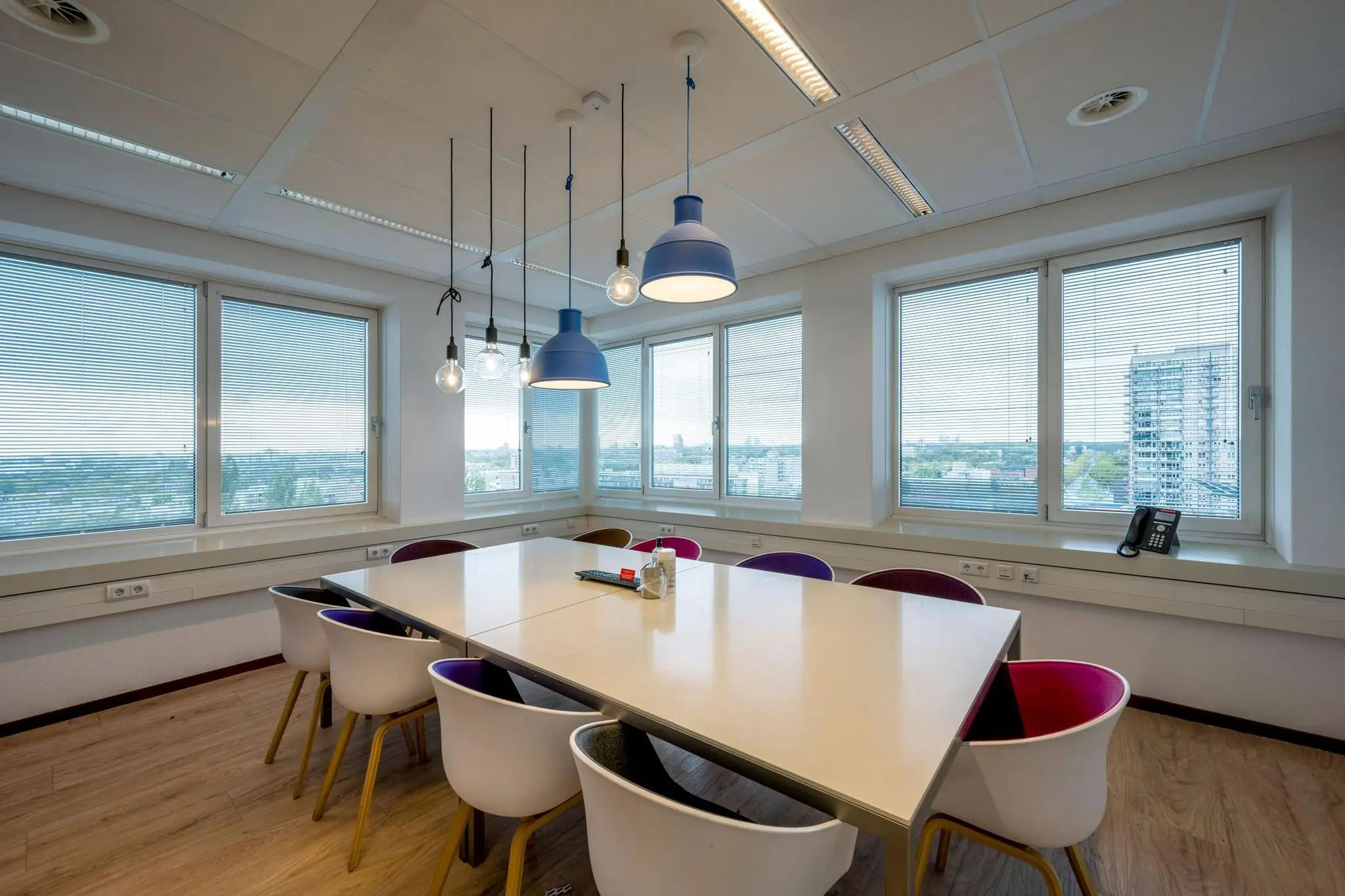 Moderne vergaderruimte aan de Watermanweg met grote ramen, kleurrijke stoelen en hanglampen.
