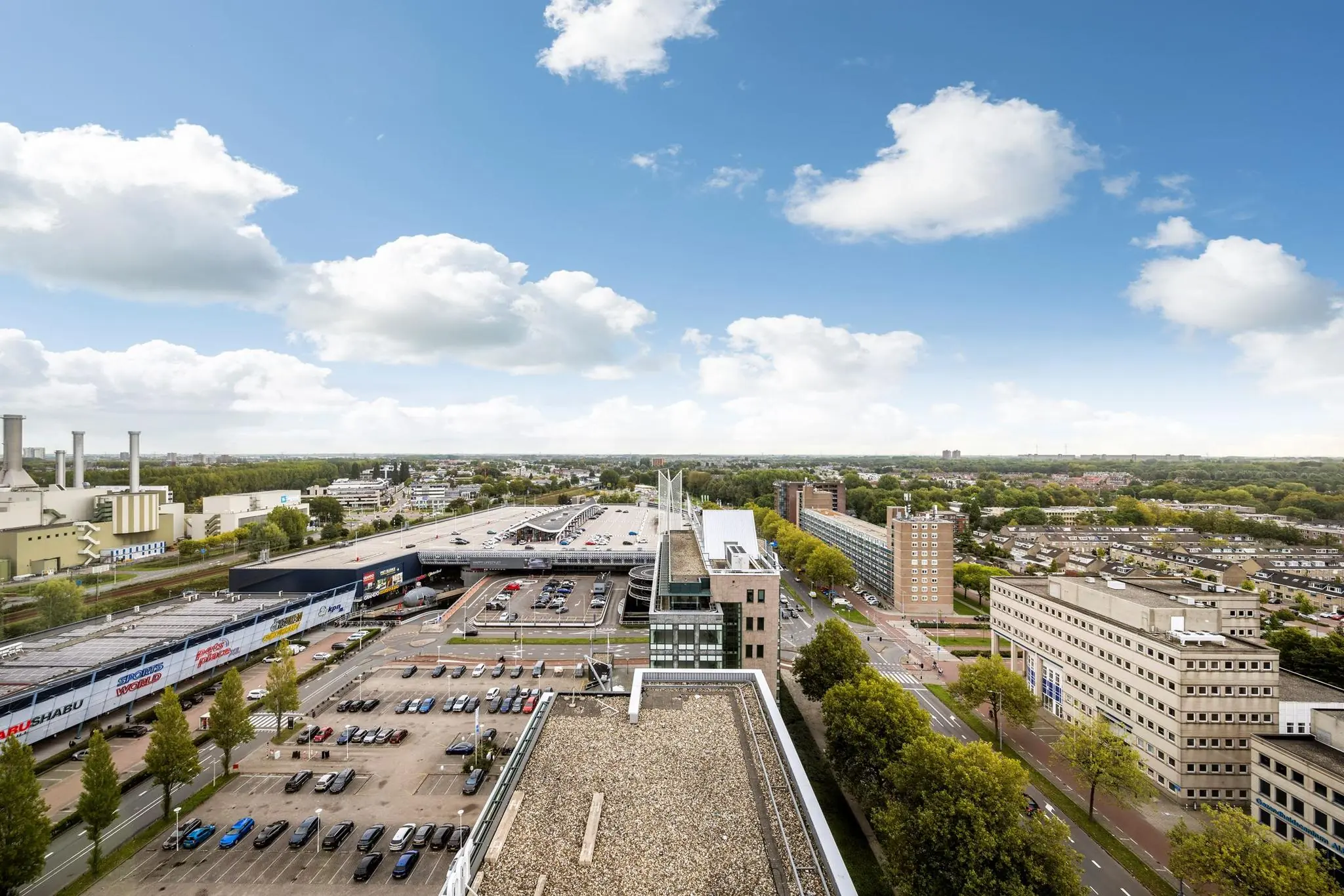 Luchtfoto van de Watermanweg in Rotterdam met parkeergarages, kantoren en woonwijken onder een deels bewolkte hemel.