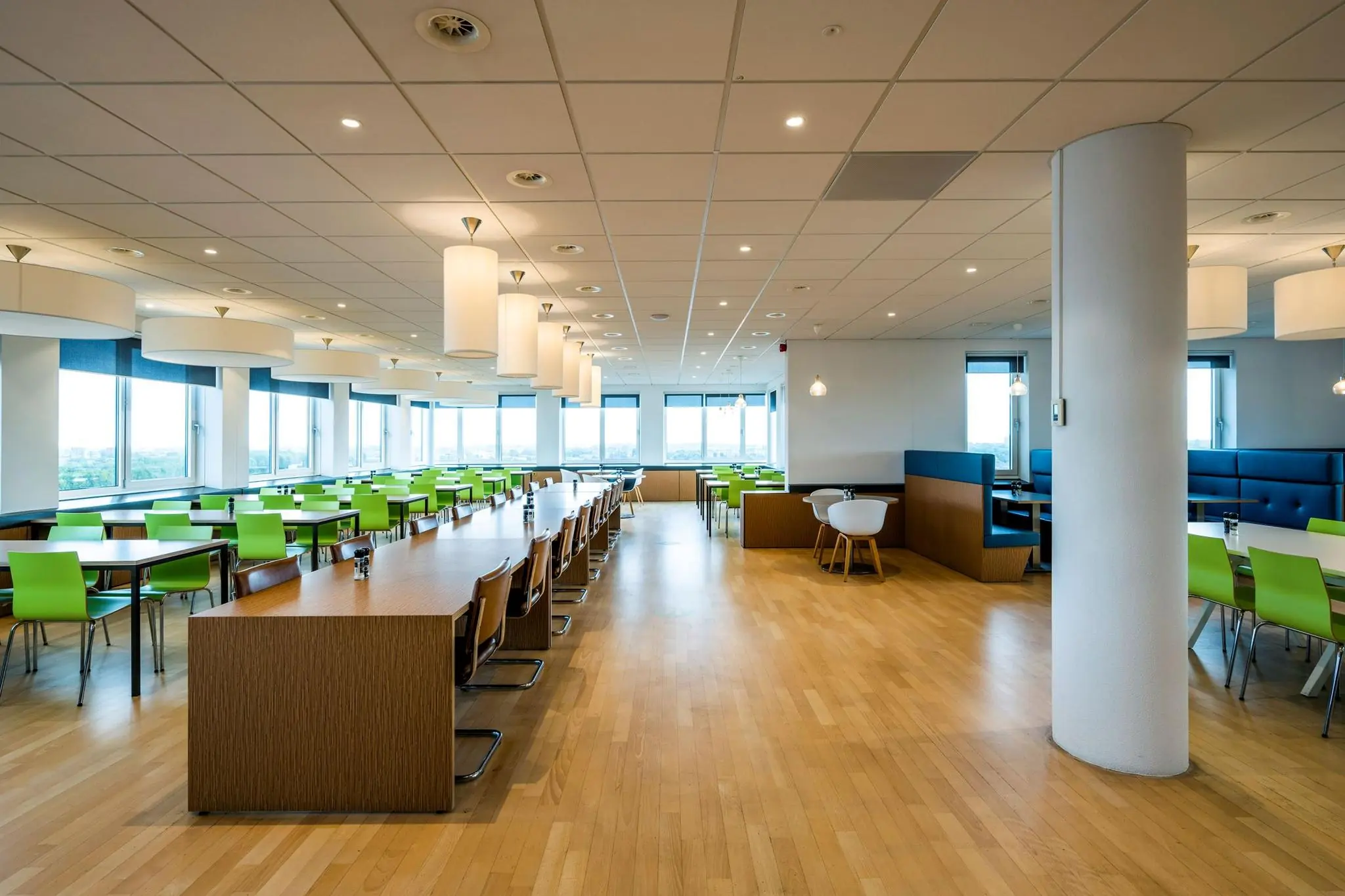 Moderne en ruime bedrijfskantine aan de Watermanweg met lange houten tafels, groene stoelen en grote ramen.
