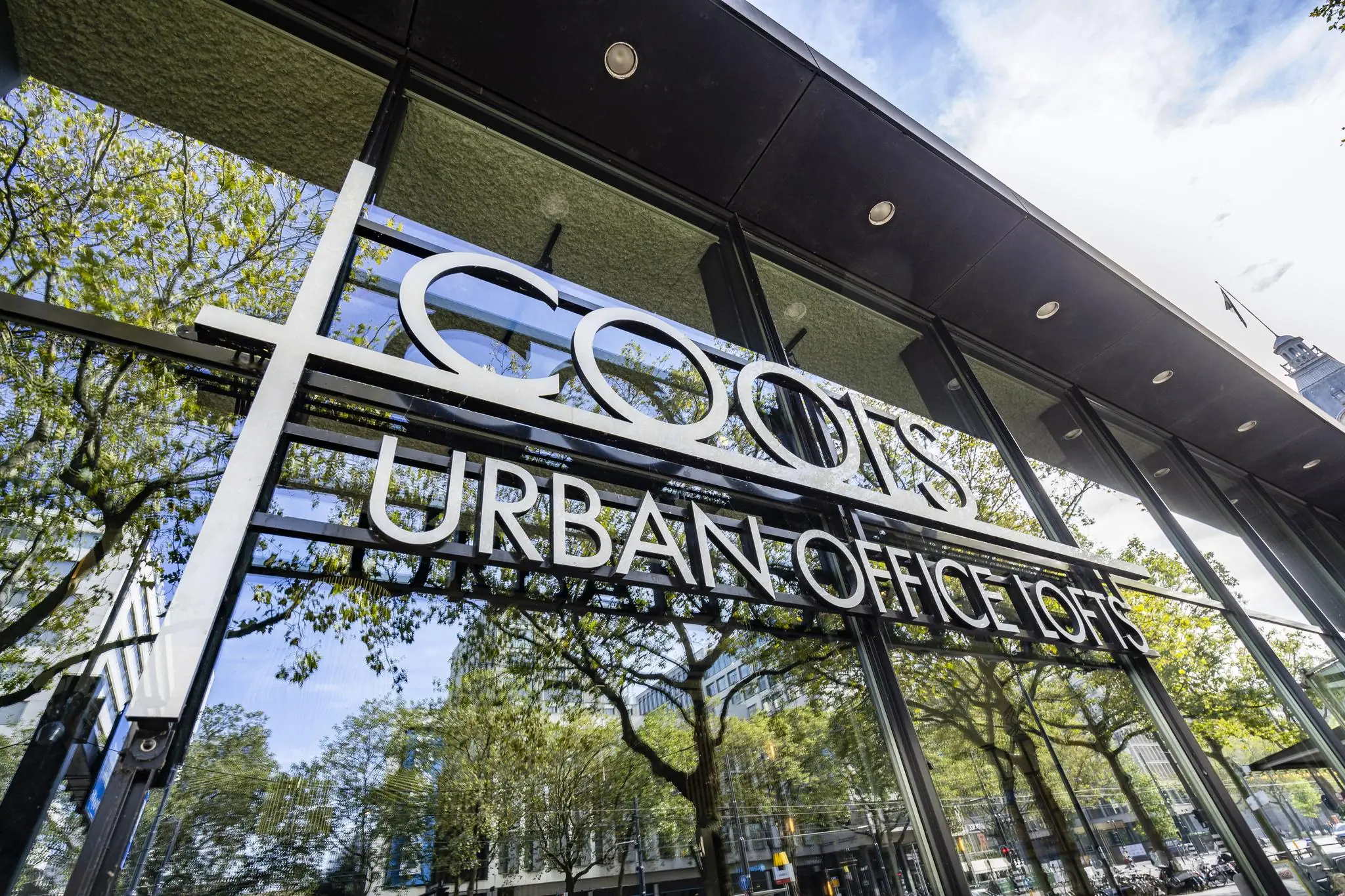 Glazen gevel van COOLS Urban Office Lofts aan de Coolsingel in Rotterdam met weerspiegeling van bomen en gebouwen.