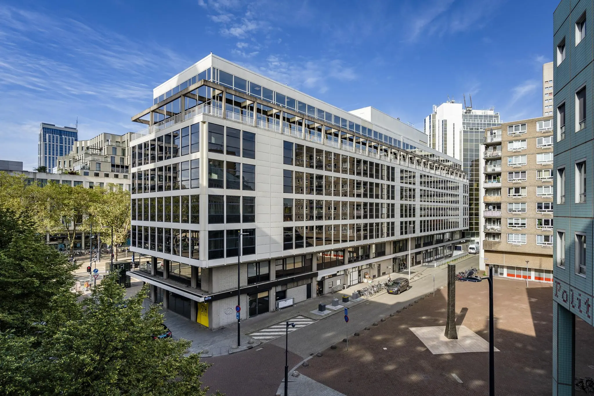 Modern kantoorgebouw aan de Coolsingel in Rotterdam met omliggende hoogbouw en een plein met kunstobject.
