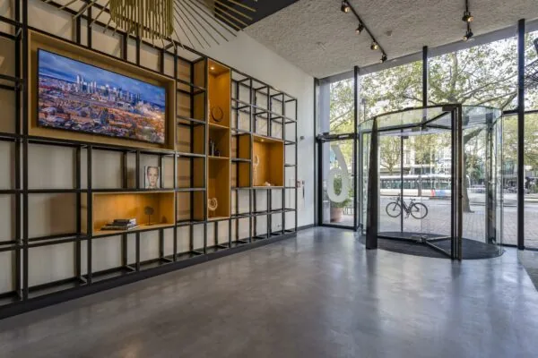 Moderne entreehal aan de Coolsingel met glazen draaideur, wanddecoratie en uitzicht op een tram en fiets buiten.