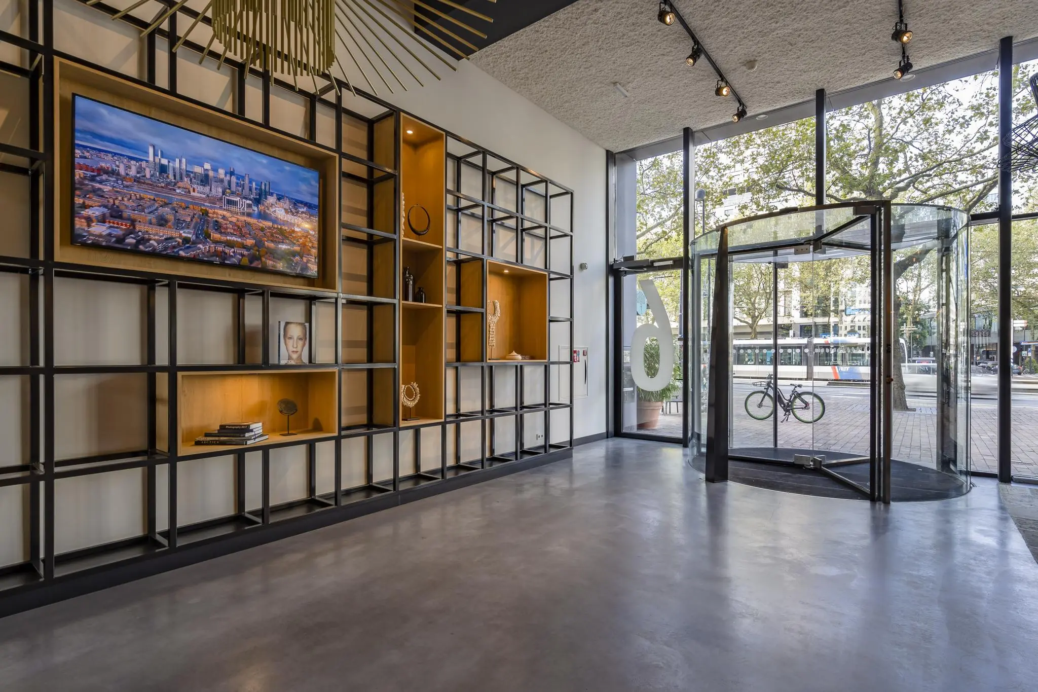 Moderne entreehal aan de Coolsingel met glazen draaideur, wanddecoratie en uitzicht op een tram en fiets buiten.