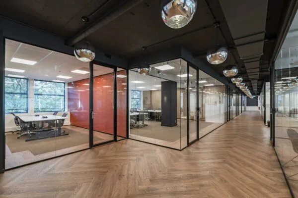 Moderne kantoorruimte aan de Coolsingel met glazen vergaderruimtes, houten visgraatvloer en industriële plafondverlichting.