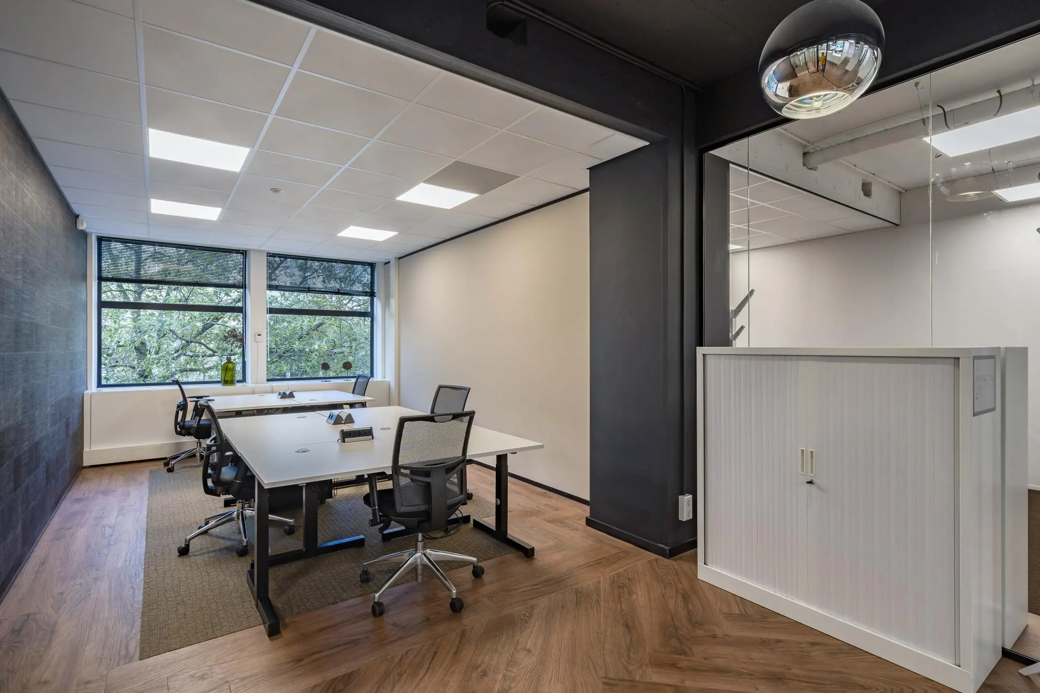 Modern ingericht kantoor aan de Coolsingel met bureaus, bureaustoelen en grote ramen met uitzicht op bomen.