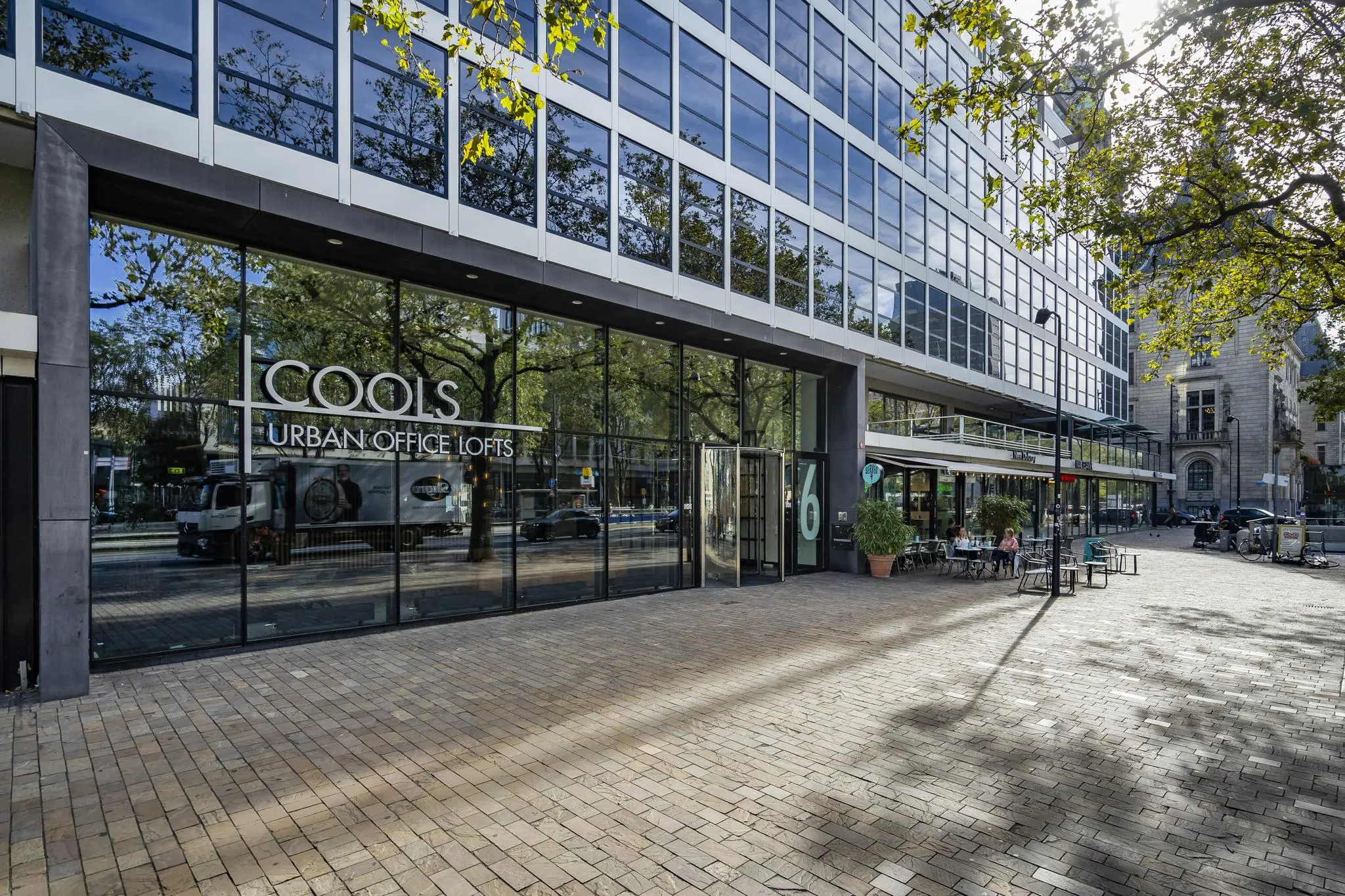 Moderne kantoorgebouw COOLS Urban Office Lofts aan de Coolsingel in Rotterdam met glazen gevel en terras met zitplaatsen.