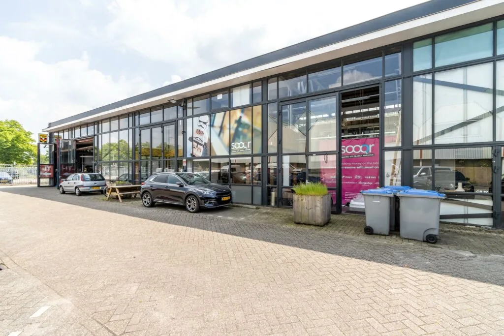 Bedrijfsgebouw aan de Eendrachtlaan met grote glazen gevel, geparkeerde auto's en zicht op het kantoor van Sooqr.