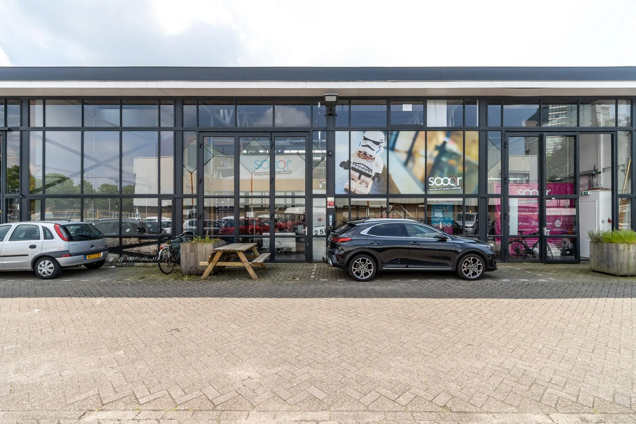 Vooraanzicht van een modern kantoorpand aan de Eendrachtlaan met geparkeerde auto's, fietsen en het logo van Sooqr.