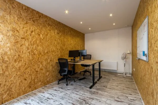 Kantoorruimte aan de Eendrachtlaan met twee bureaus, computerschermen, houten OSB-wanden en een whiteboard.