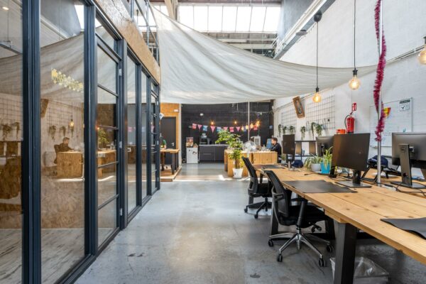 Open en creatief ingericht kantoor aan de Eendrachtlaan met houten bureaus, planten en hangende verlichting.