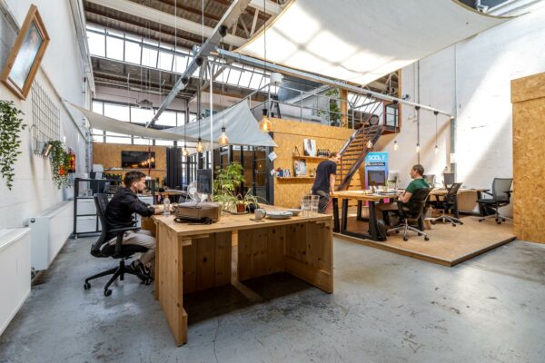 Moderne, industriële kantoorspace aan de Eendrachtlaan met houten meubels, hoge plafonds en werkende mensen aan bureaus.