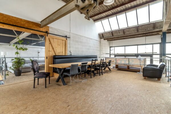 Industriële vergaderruimte op de Eendrachtlaan met houten tafel, diverse stoelen en grote ramen voor natuurlijk licht.