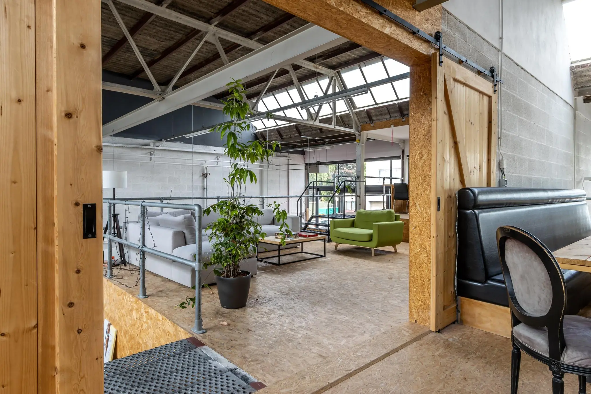 Industriële en modern ingerichte zithoek in een kantoorruimte aan de Eendrachtlaan met zicht op een groene fauteuil en grote dakramen.