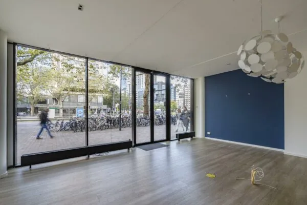 Leegstaand winkel- of kantoorpand met grote glazen pui aan de Coolsingel in Rotterdam, met uitzicht op voorbijgangers en fietsenrekken.