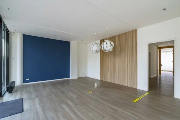 Leeg modern interieur aan de Coolsingel met houten vloer, blauwe accentmuur en decoratieve hanglampen.