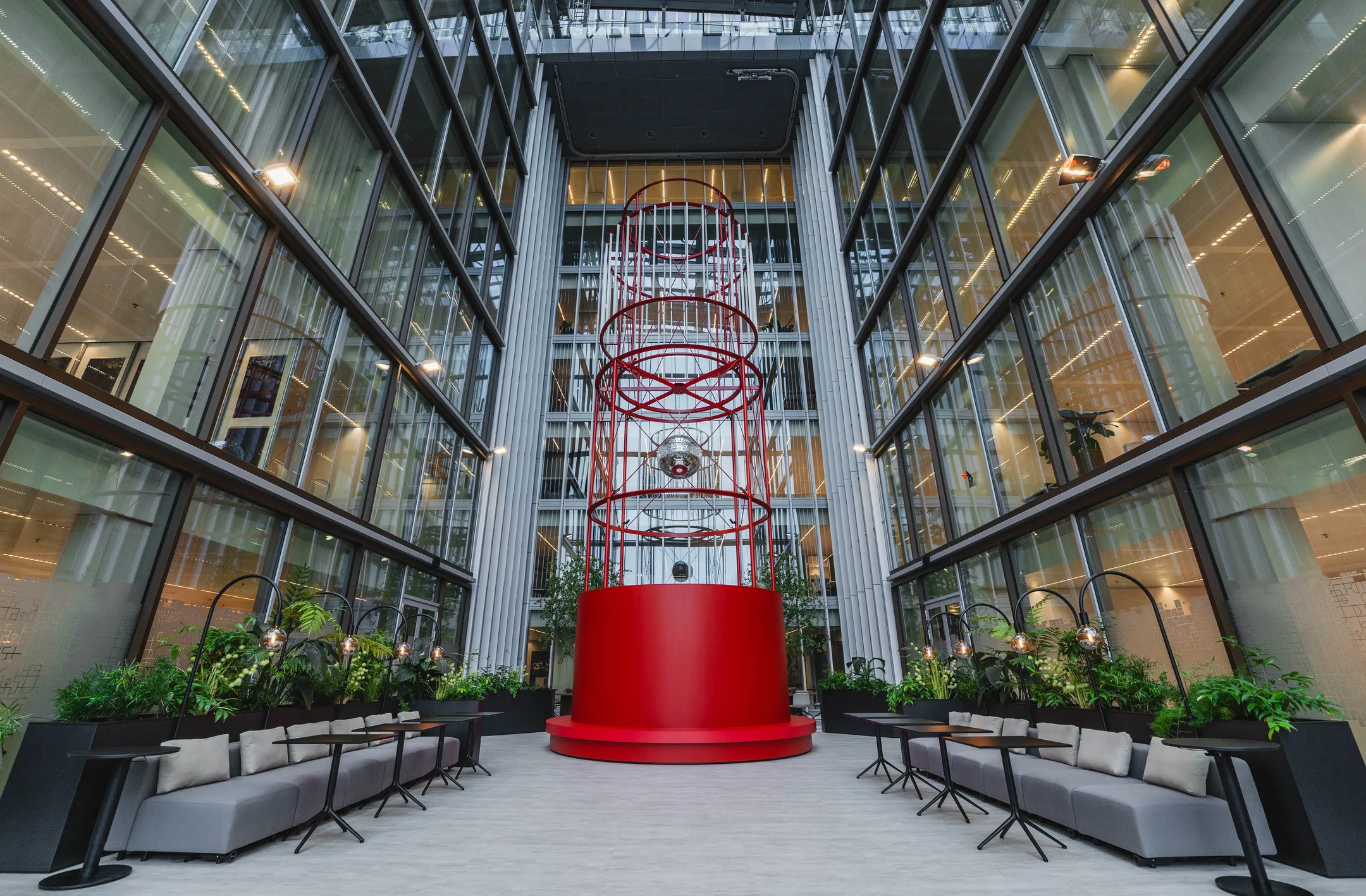 Interieur van een modern atrium met een opvallende rode sculptuur en zitplaatsen aan weerszijden.