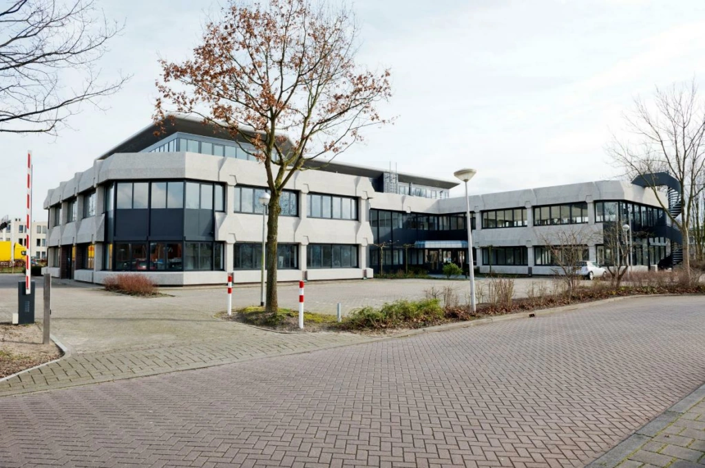 Kantoorgebouw aan de Wattbaan met modern ontwerp en ruime parkeerplaats op de voorgrond.