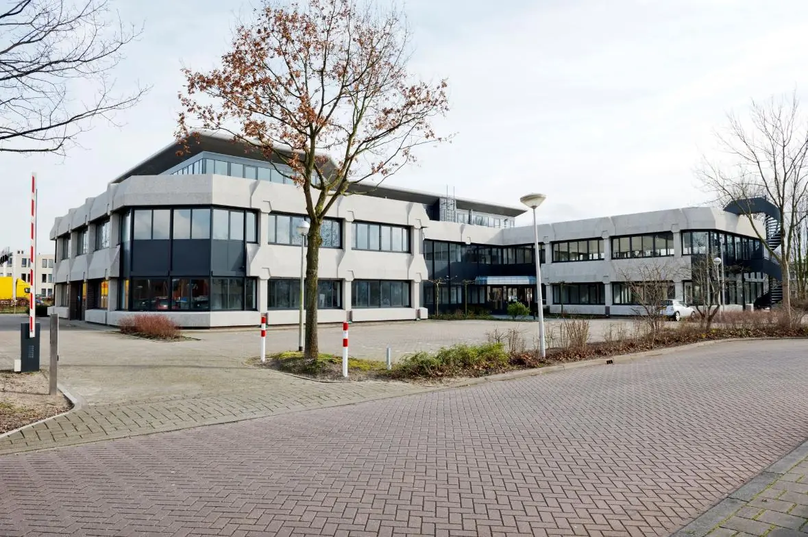 Kantoorgebouw aan de Wattbaan met modern ontwerp en ruime parkeerplaats op de voorgrond.