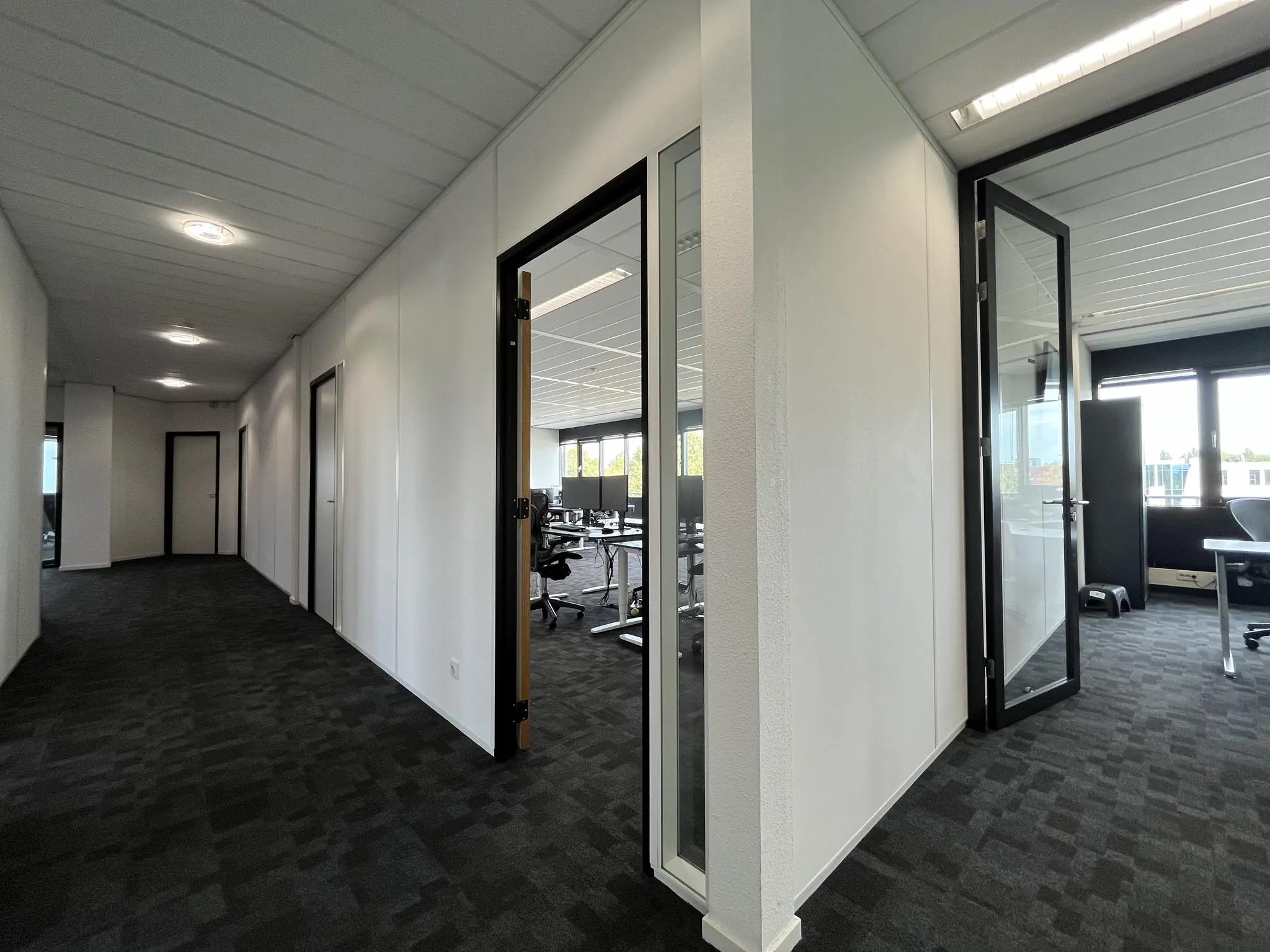 Gang met openstaande deuren naar moderne kantoorkamers in een bedrijfsverzamelgebouw aan de Wattbaan.