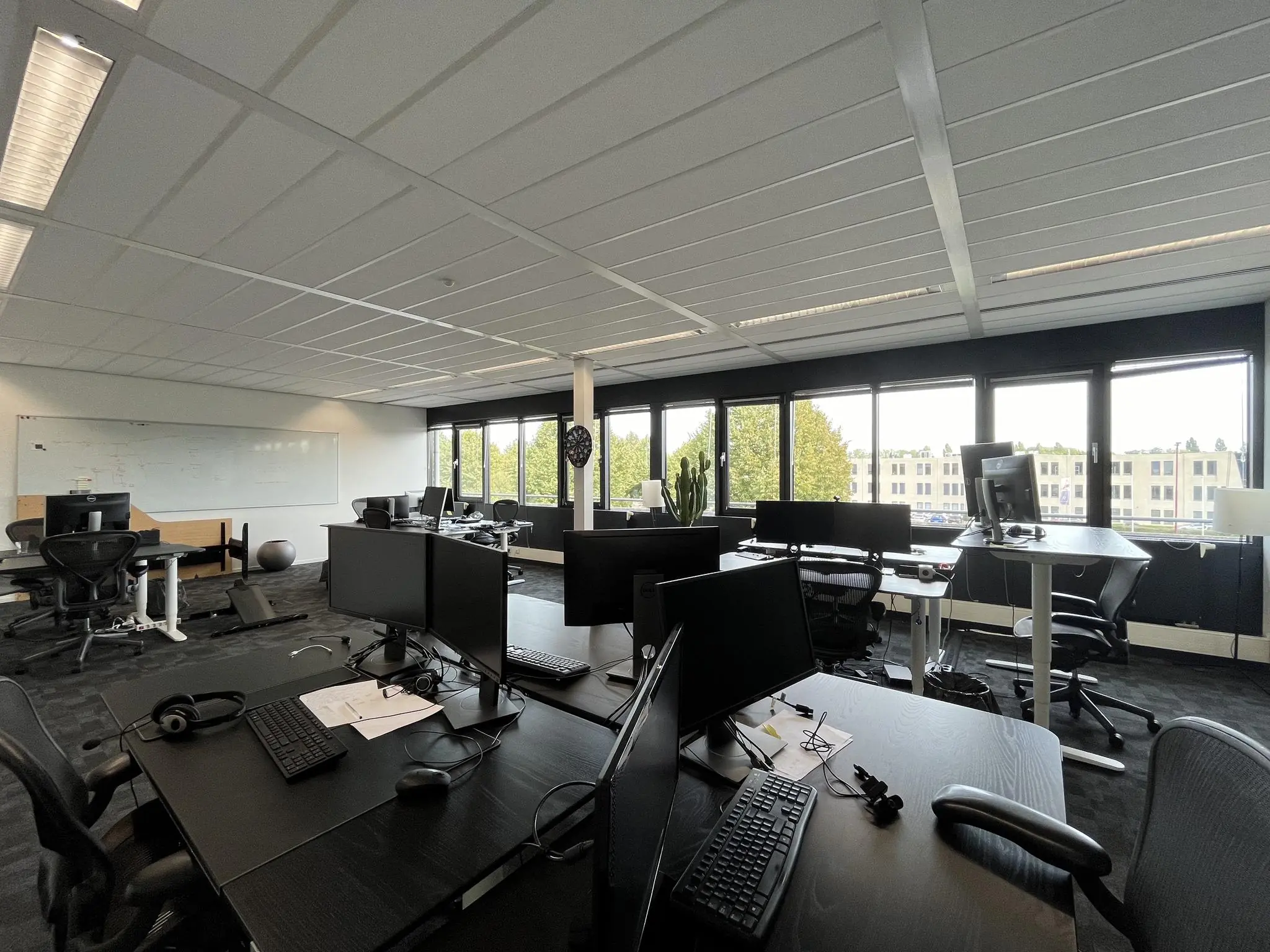 Moderne kantooruimte aan de Wattbaan met meerdere werkplekken, grote ramen en uitzicht op een gebouw buiten.