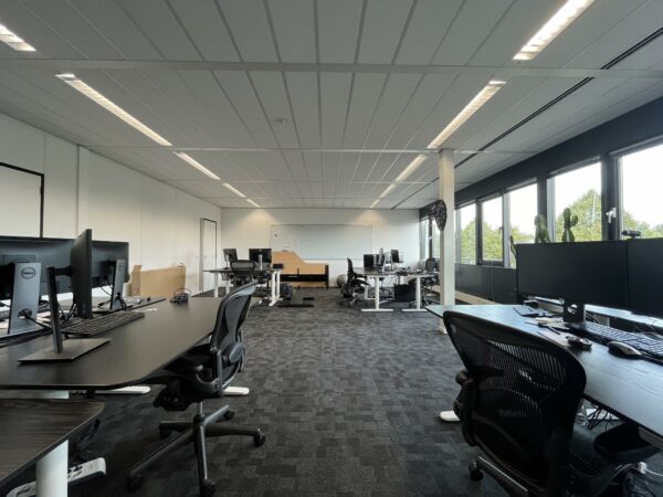 Moderne, open kantoorruimte aan de Wattbaan met meerdere bureaus, computerschermen en grote ramen met uitzicht op groen.