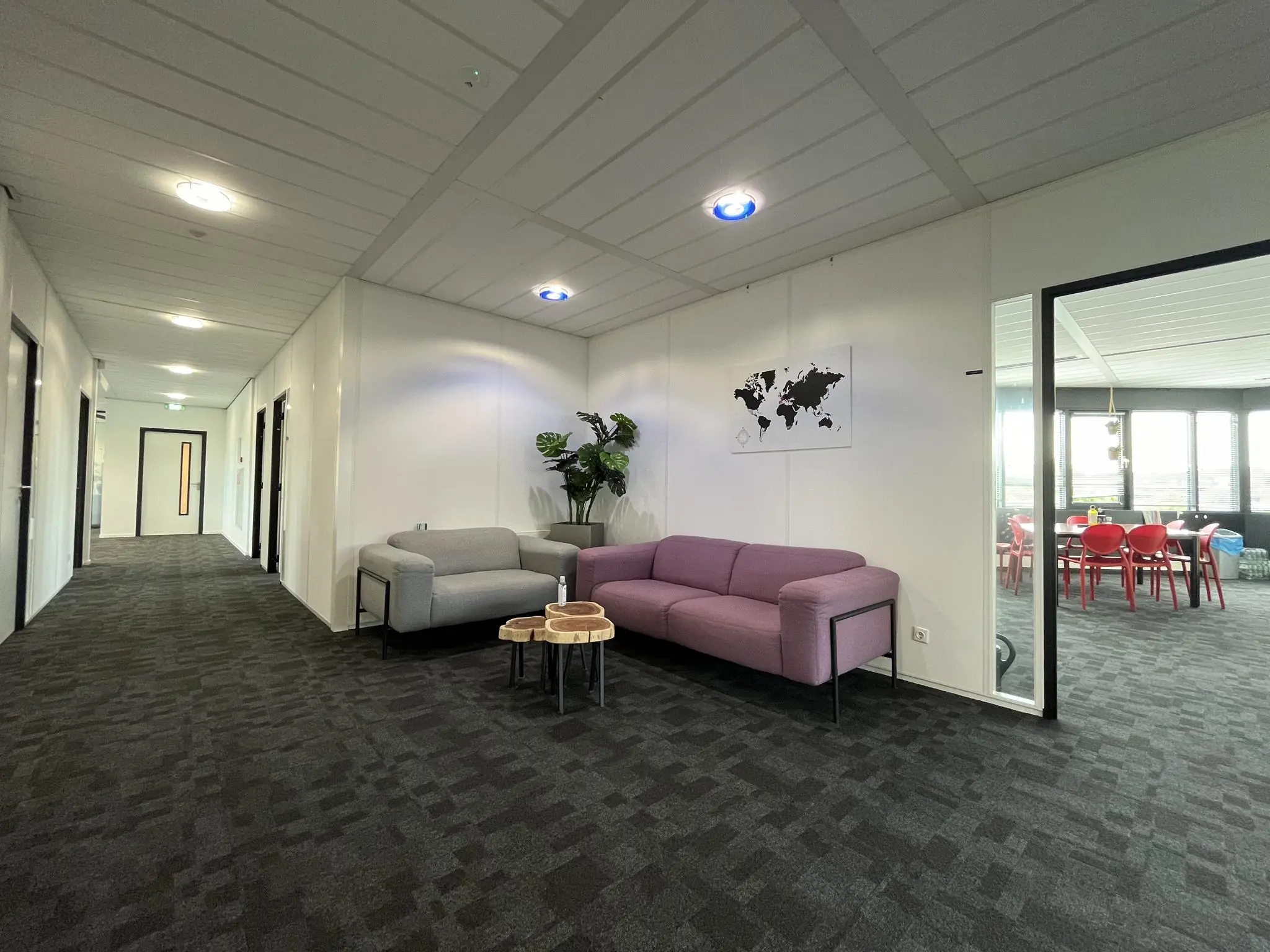 Moderne kantoorhal met zithoek, wereldkaart aan de muur en zicht op vergaderruimte met rode stoelen.