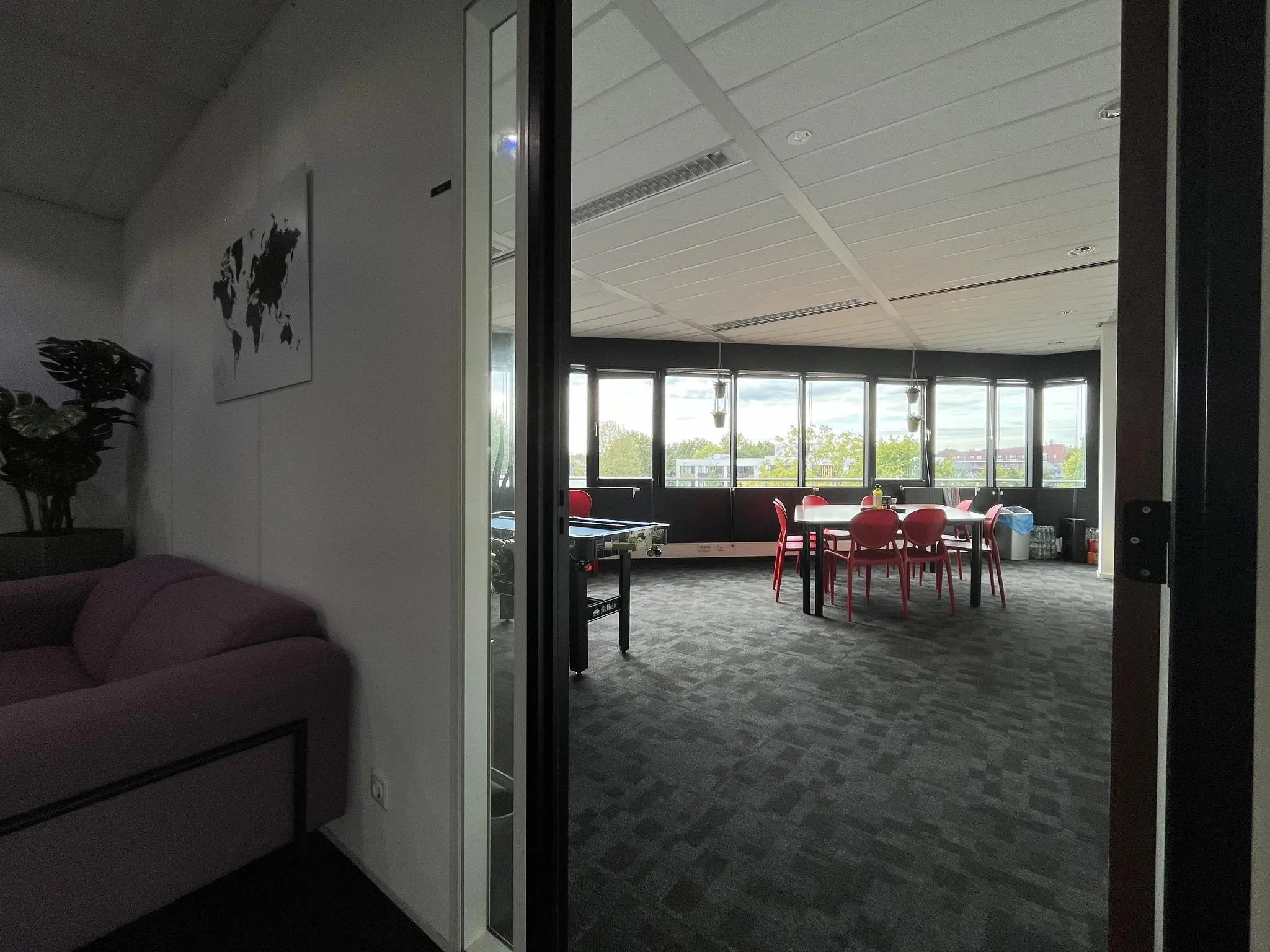 Kantoorruimte met grote ramen, een vergadertafel met rode stoelen en een loungehoek met paarse bank.