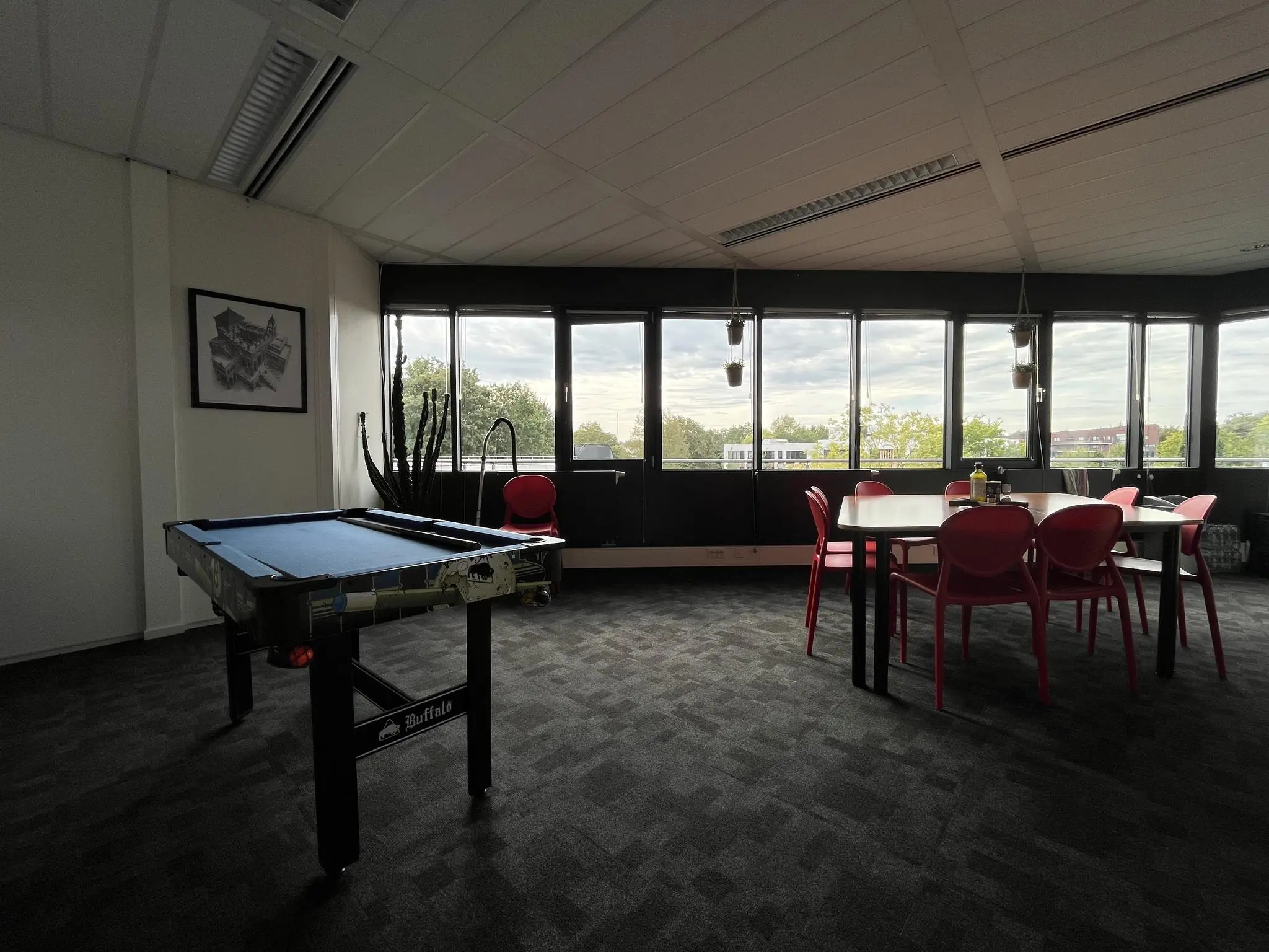 Kantineruimte op Wattbaan met pooltafel, rode stoelen en grote ramen met uitzicht op groen.