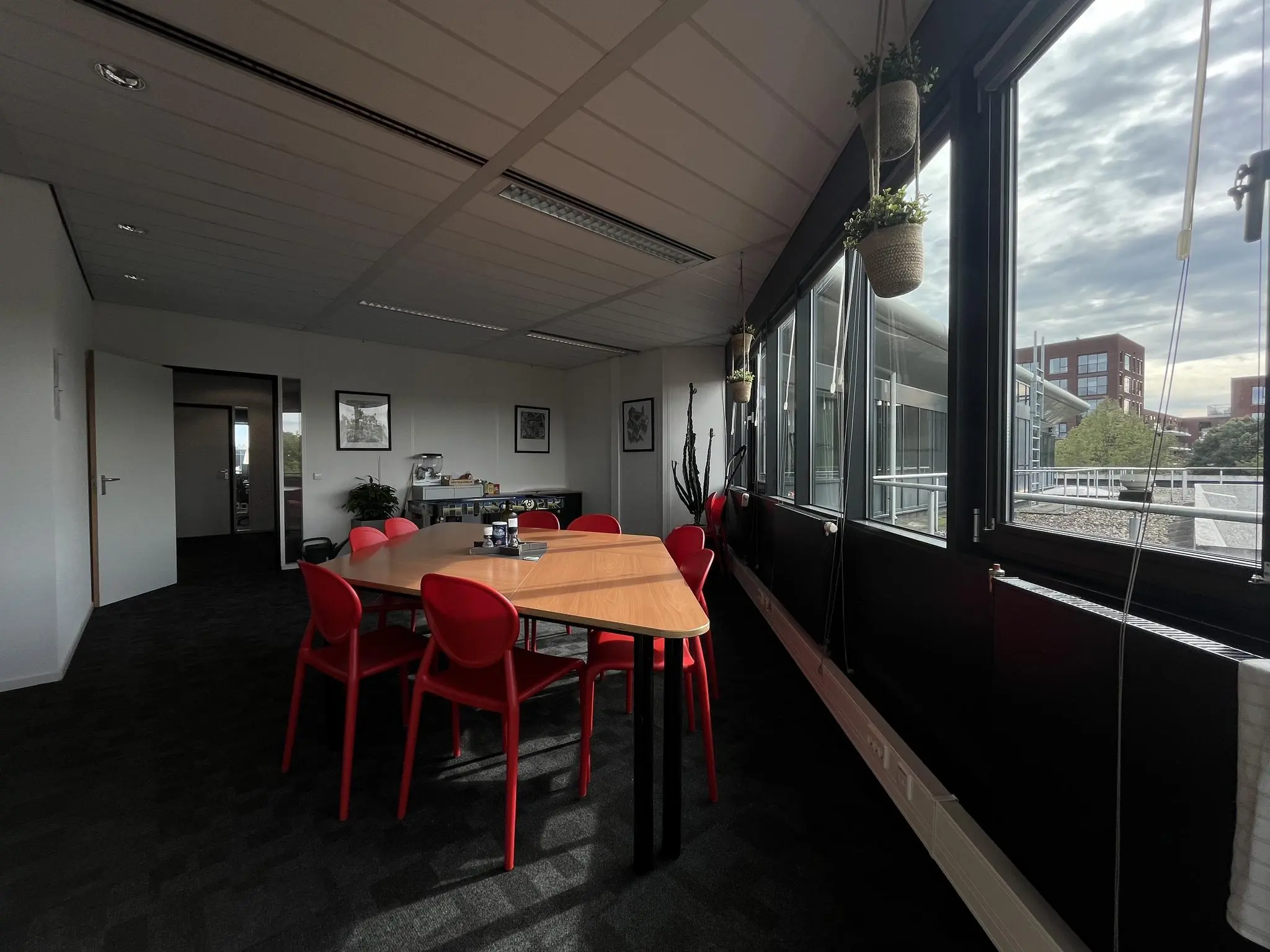 Vergaderruimte met rode stoelen, houten tafel en grote ramen aan de Wattbaan met uitzicht op moderne kantoorgebouwen.