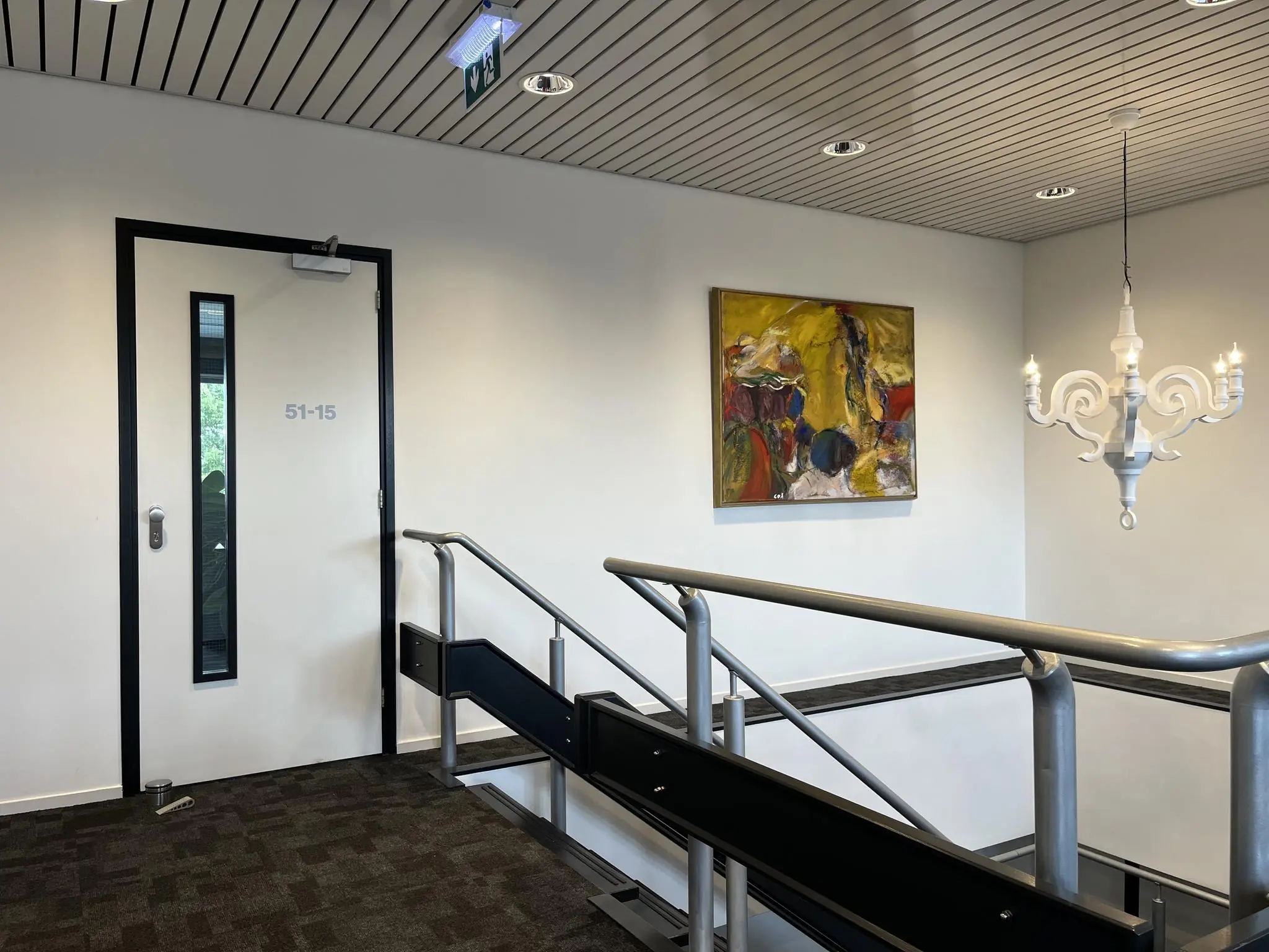 Moderne kantoorhal met deur 51-15, abstract schilderij aan de muur en een witte kroonluchter boven de trap.