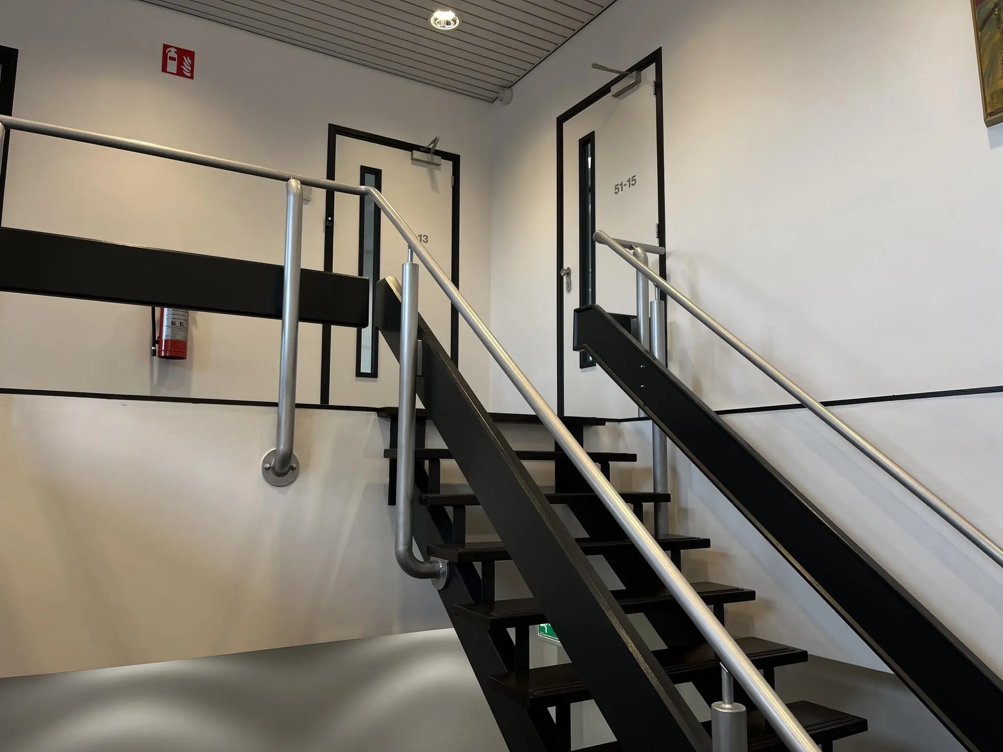Interieur van een trappenhuis op de Wattbaan met zwarte traptreden, metalen leuningen en deuren genummerd 13 en 51-15.