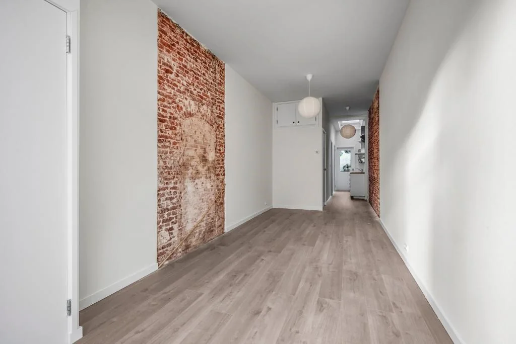 Langwerpige gang met houten vloer, witte muren en decoratieve bakstenen accenten in een woning aan de Westerstraat.