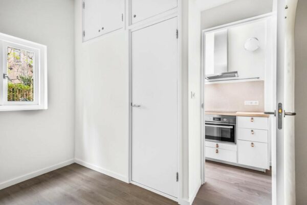 Licht interieur met witte kasten en een doorkijk naar een moderne keuken in een woning aan de Westerstraat.