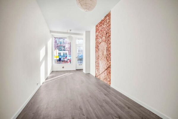 Lichte, smalle kamer met houten vloer, witgestucte muren en een decoratieve bakstenen muurfoto aan de rechterzijde, gelegen aan de Westerstraat.