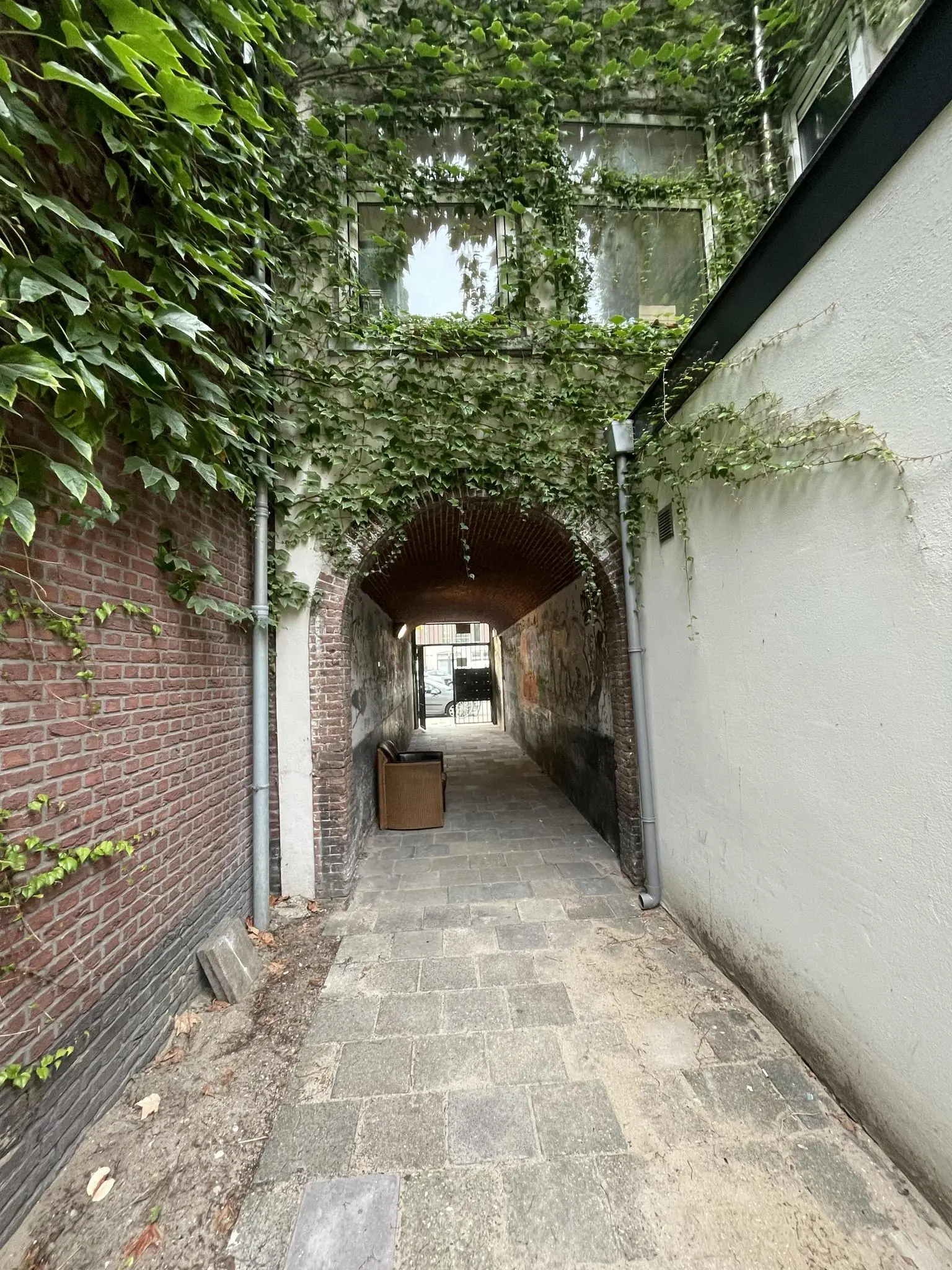 Smal steegje aan de Westerstraat met overgroene gevels, een boogdoorgang en een oude stoel op de achtergrond.