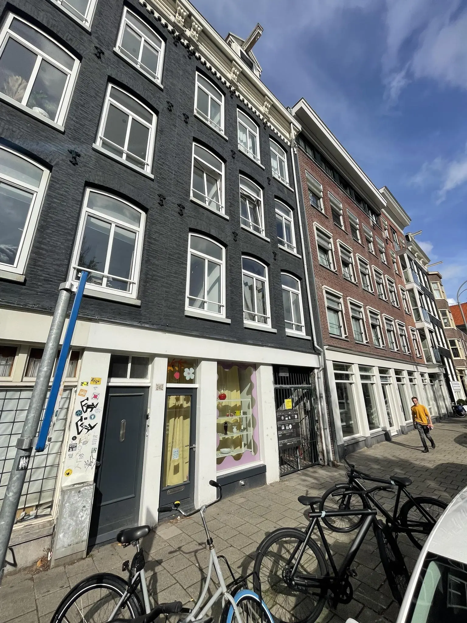 Voorgevel van een zwart geschilderd pand aan de Westerstraat in Amsterdam met fietsen op de stoep en een wandelende man.