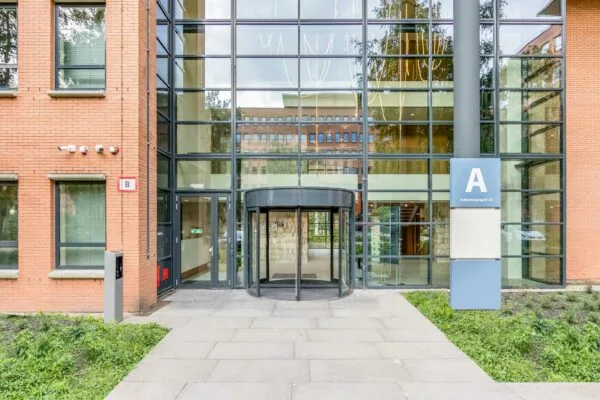 Ingang van een kantoorgebouw aan de Hullenbergweg met een grote glazen gevel, een draaideur en aanduidingen voor gebouwen A en B.