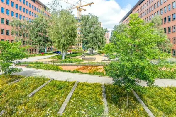 Groene binnentuin met bankjes en bomen tussen rode kantoorgebouwen aan de Hullenbergweg.