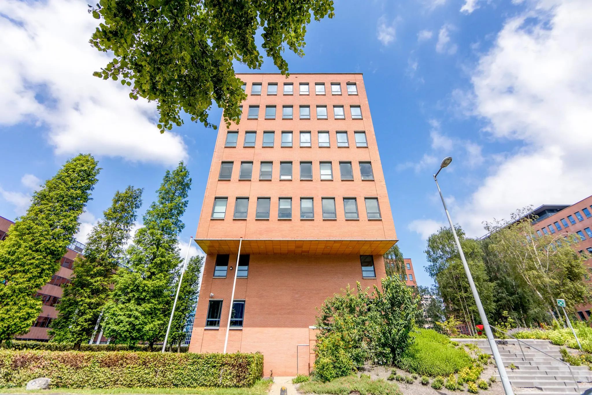 Kantoorgebouw aan de Hullenbergweg met rode bakstenen gevel, omgeven door groen en trappen.