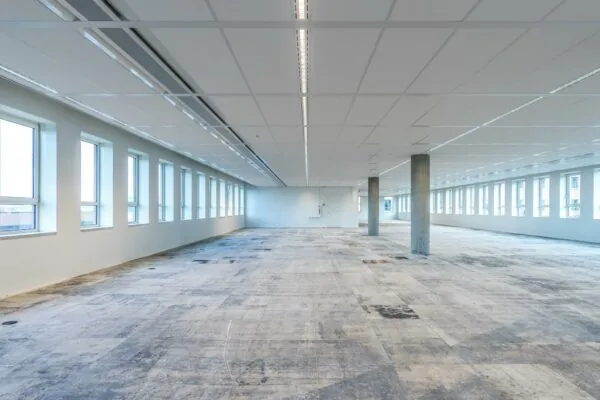 Leeg kantoorpand aan de Hullenbergweg met grote ramen en een onafgewerkte vloer.