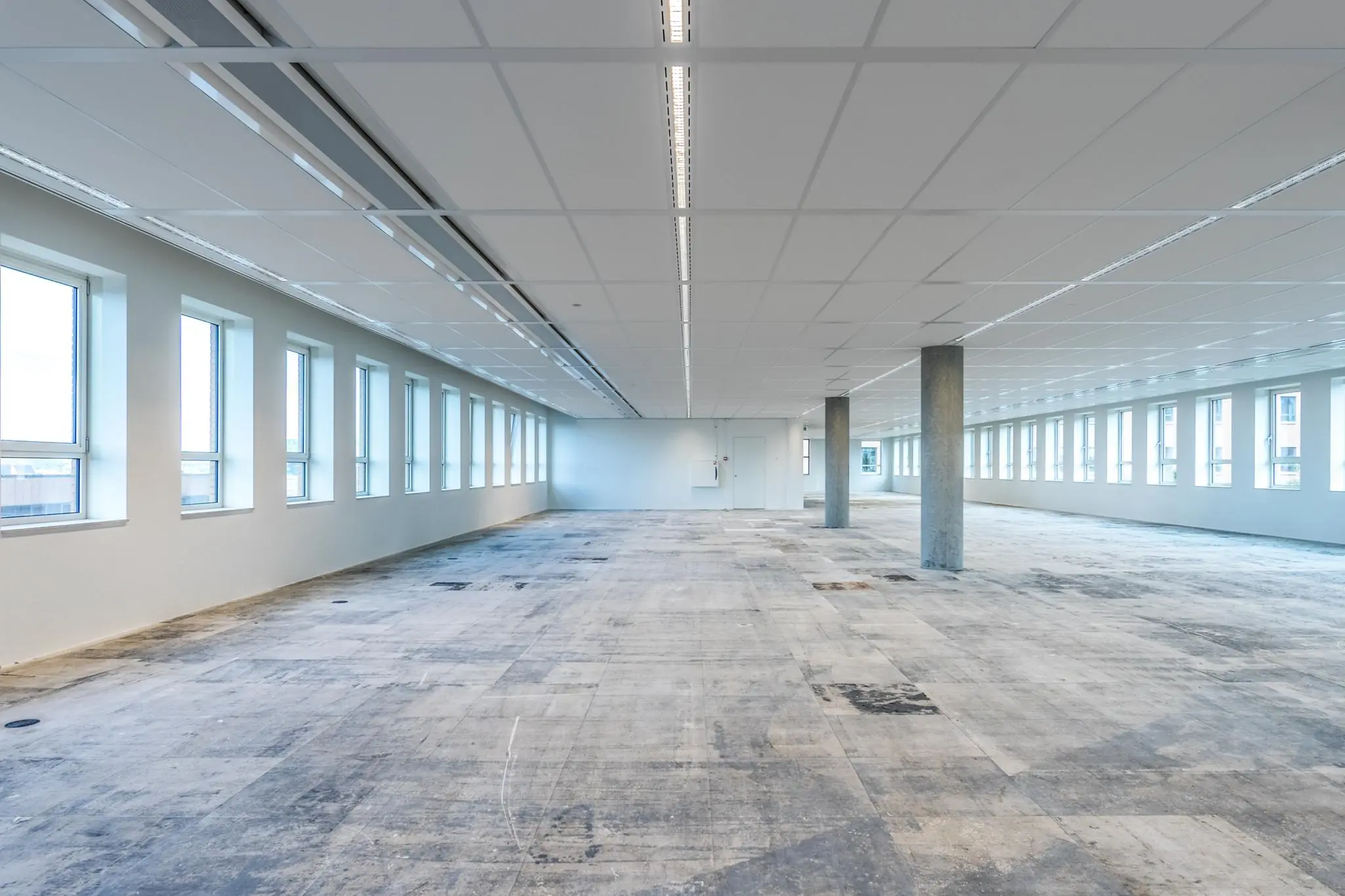 Leeg kantoorpand aan de Hullenbergweg met grote ramen en een onafgewerkte vloer.