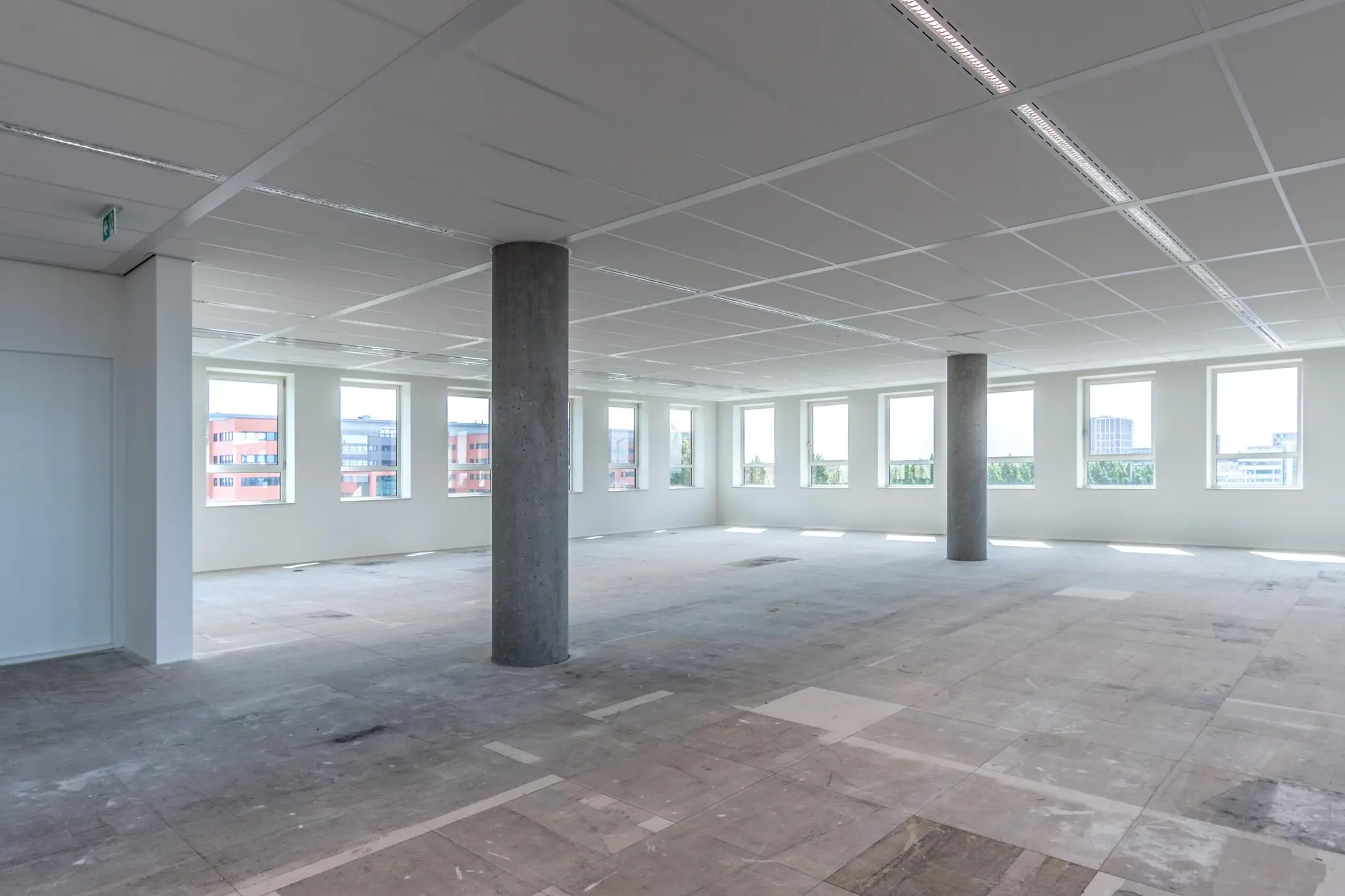 Leeg kantoorpand aan de Hullenbergweg met betonnen vloer, systeemplafond en ramen rondom.