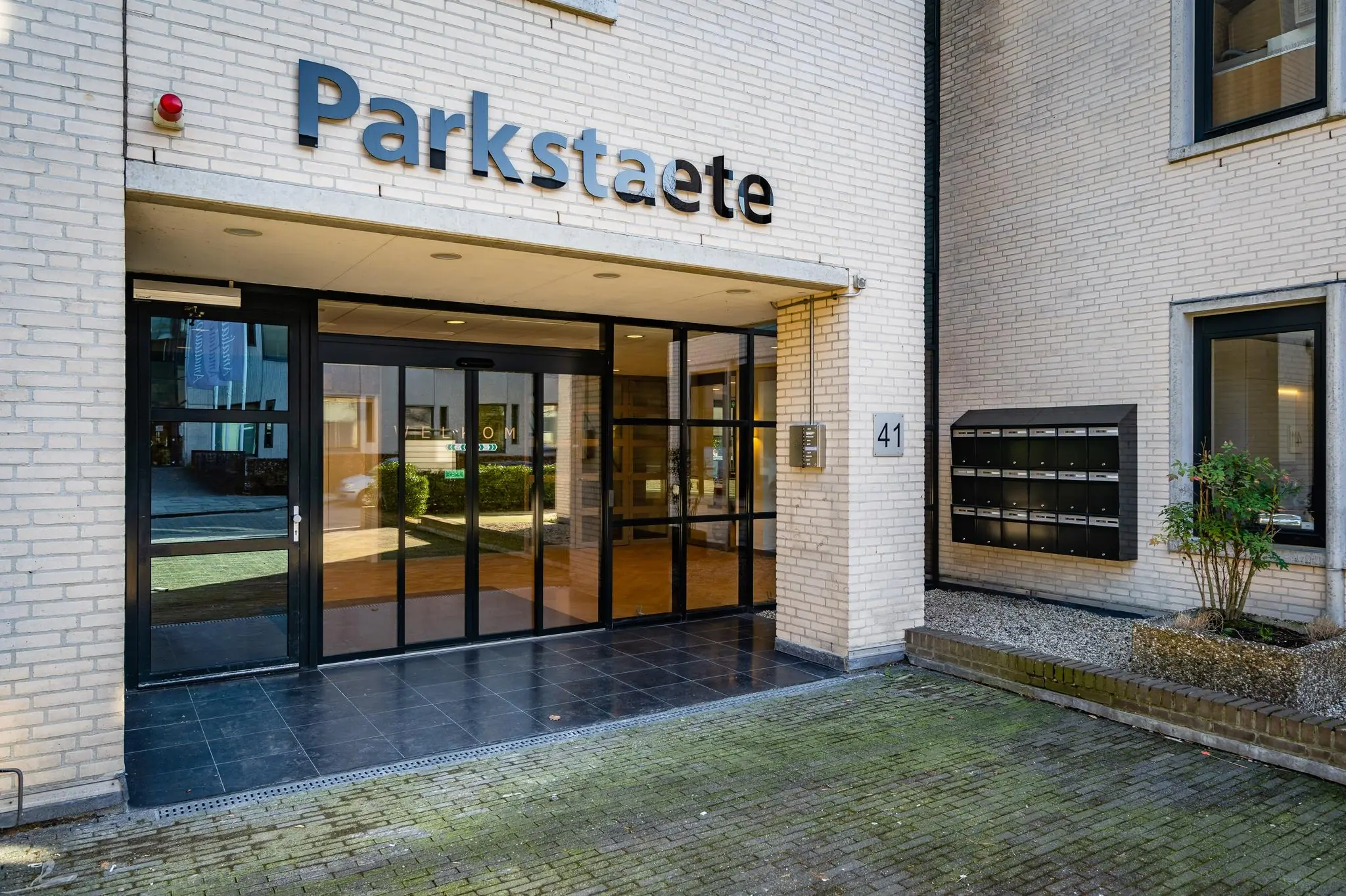 Ingang van het gebouw Parkstaete aan de Amaliastraat 41 met glazen schuifdeuren en brievenbussen.