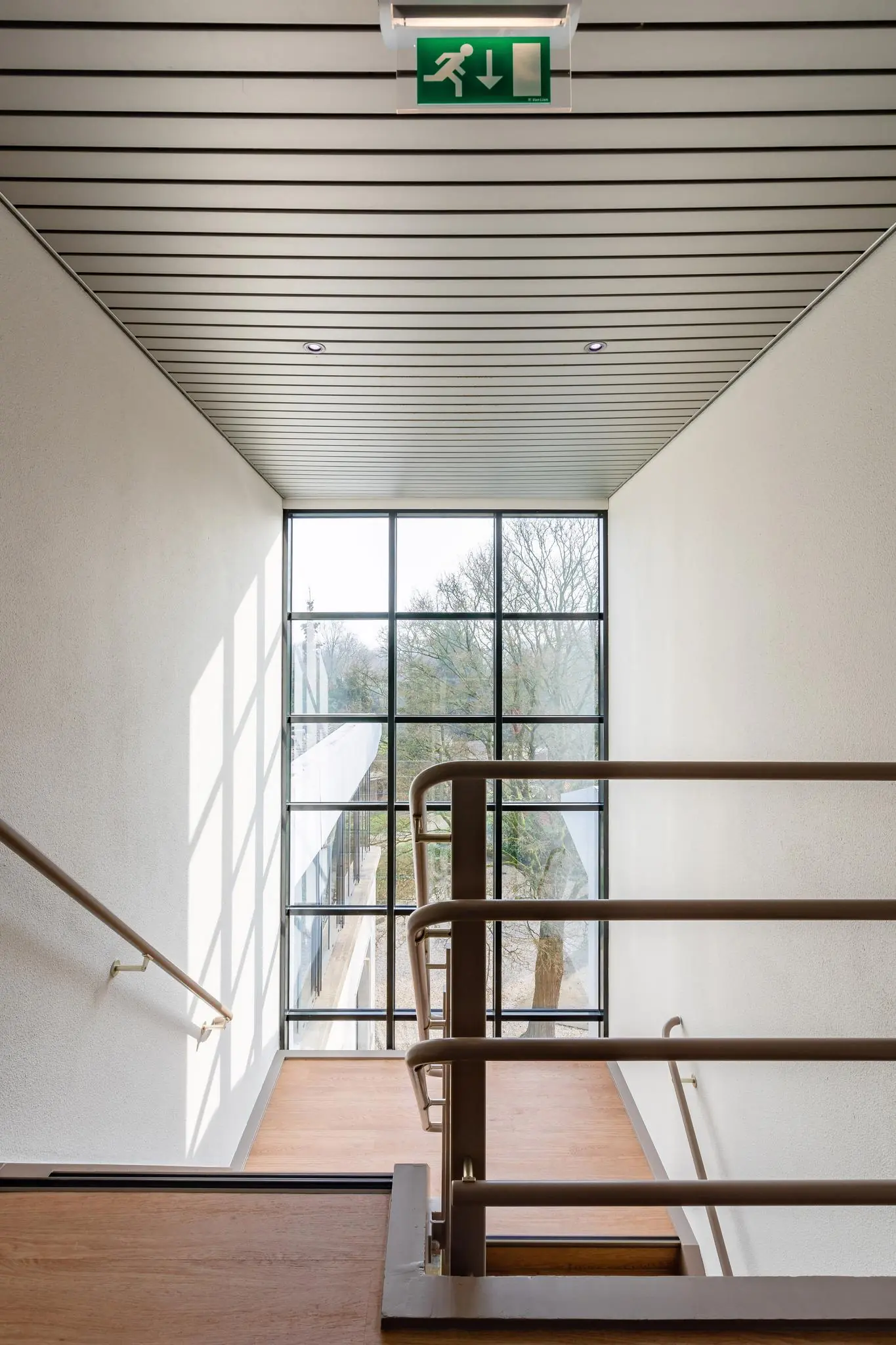 Trappenhuis in een modern gebouw aan de Amalia­laan met grote raampartij en duidelijk zichtbaar nooduitgangsbord aan het plafond.