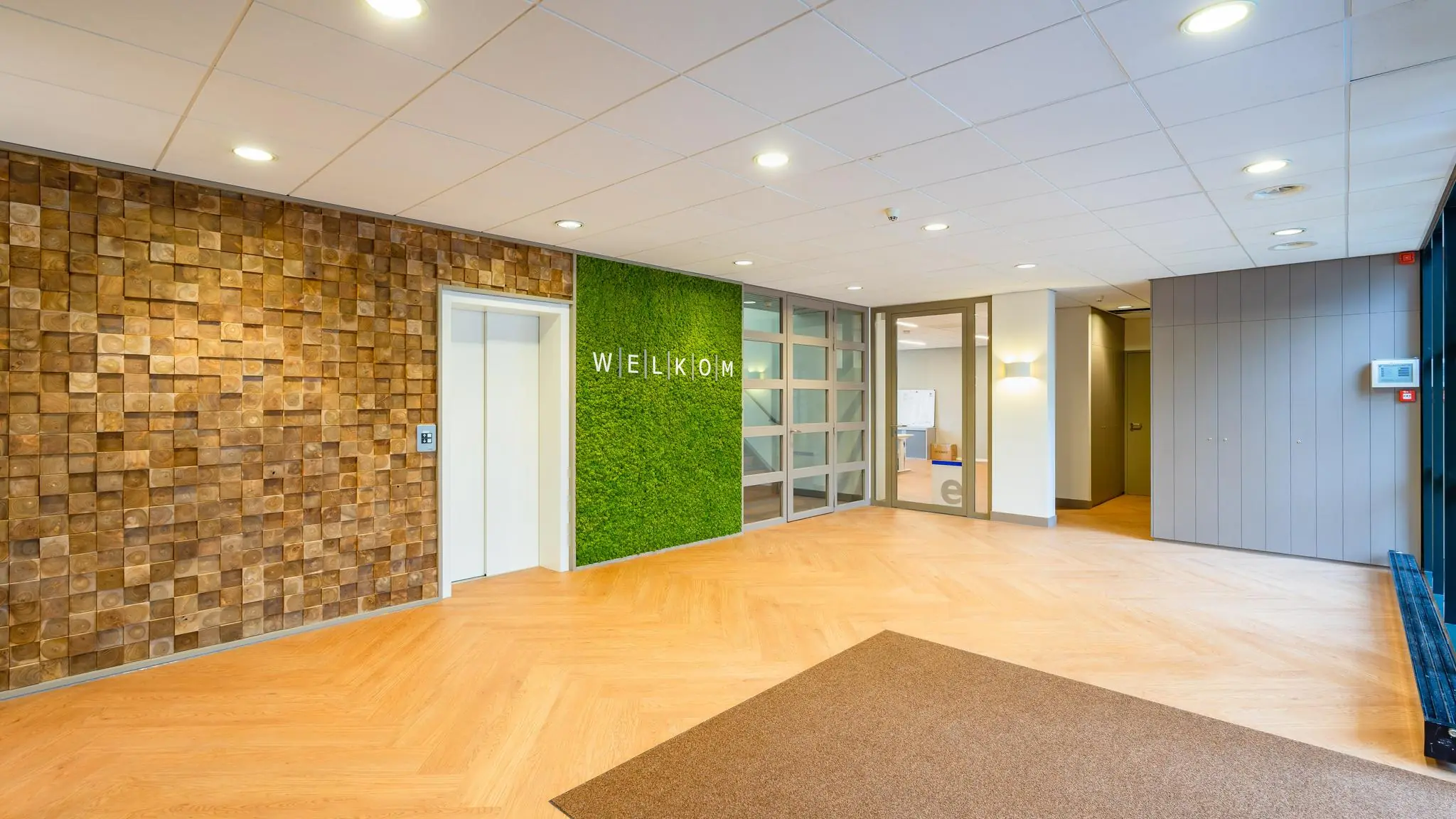 Moderne en sfeervolle entree van een kantoorpand aan de Amaliastraat met groenemuur en houten accenten.