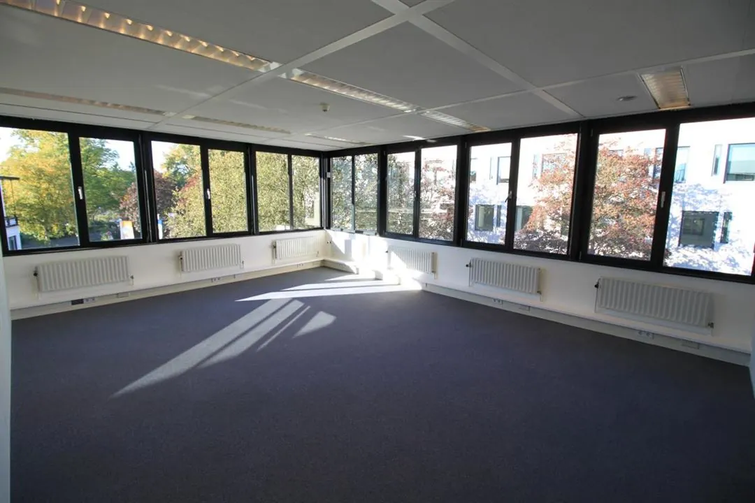 Lichte, lege kantoorruimte aan de Amalialaan met grote ramen en uitzicht op bomen.