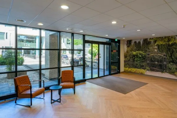 Moderne entree met zithoek, glazen gevel, en een muurfoto van het toegangshek tot Amalia Park.