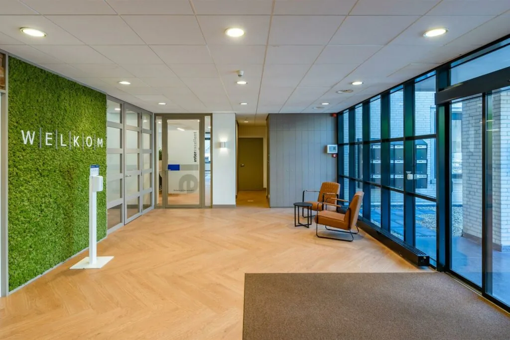 Moderne entreehal aan de Amaliastaat met groene wand, ontvangstbalie en zithoek bij grote ramen.