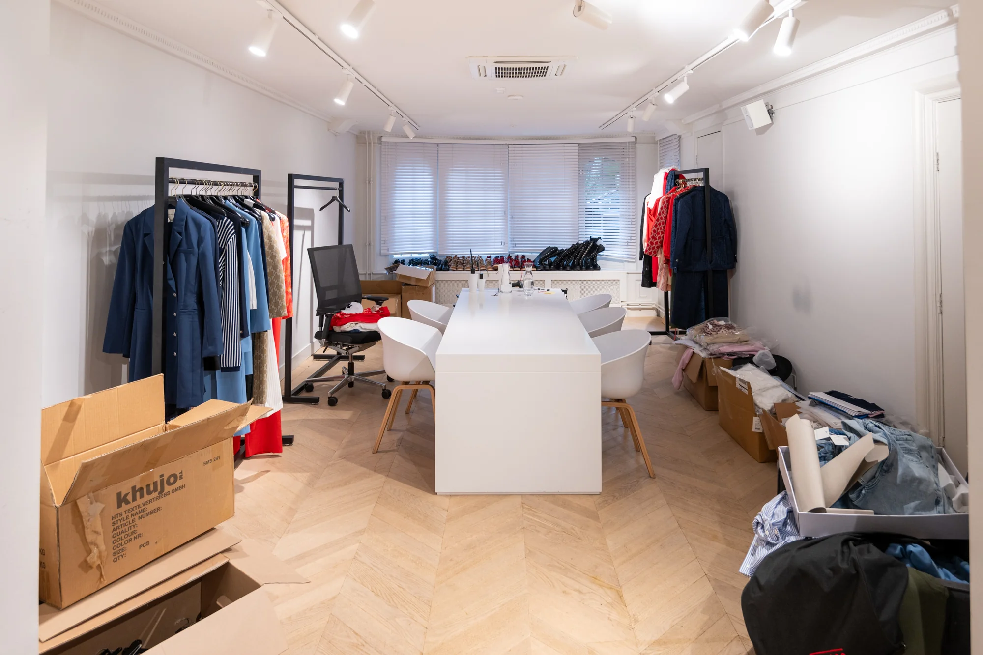 Vergaderruimte aan de Hobbemastraat ingericht als showroom met kledingrekken, dozen en kledingstukken.