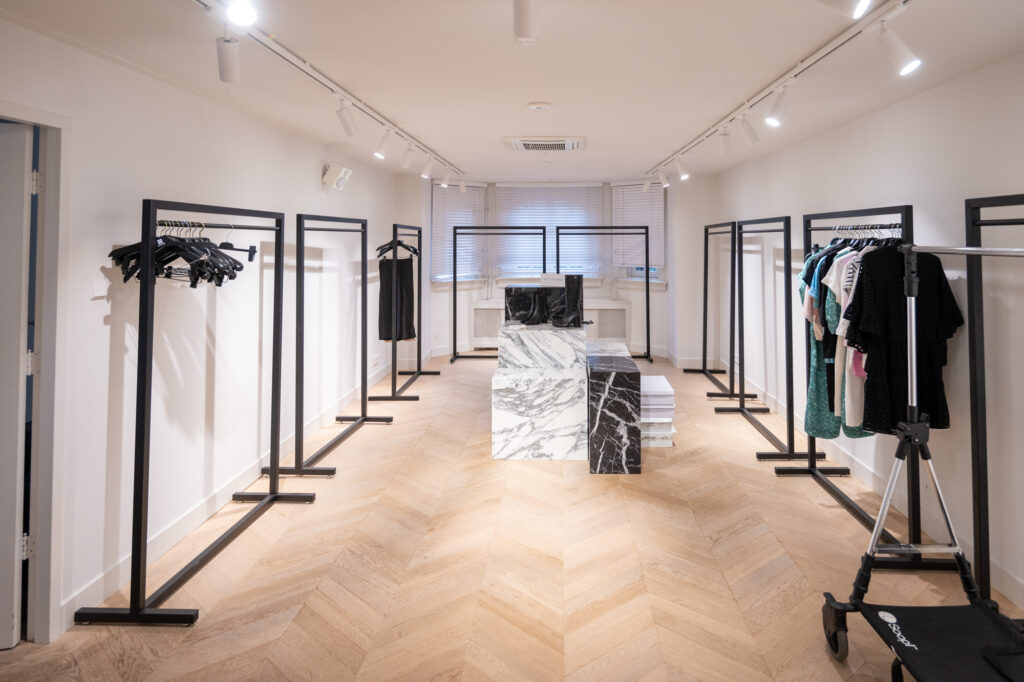 Minimalistisch ingerichte kledingwinkel aan de Hobbemastraat met zwarte kledingrekken en een marmeren toonbank.